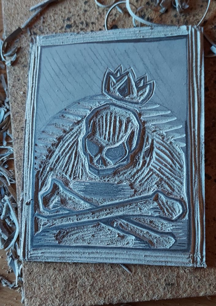 Plaque de lino avec un dessin d’un crâne flottant au-dessus de 2 fémurs croisés, et surmonté d’une couronne, version gravée