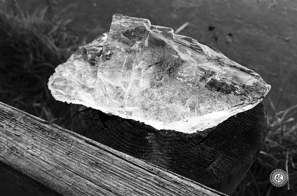 Photo noir et blanc d’un morceau de glace pareil du cristal brut, posé sur poteau en bois